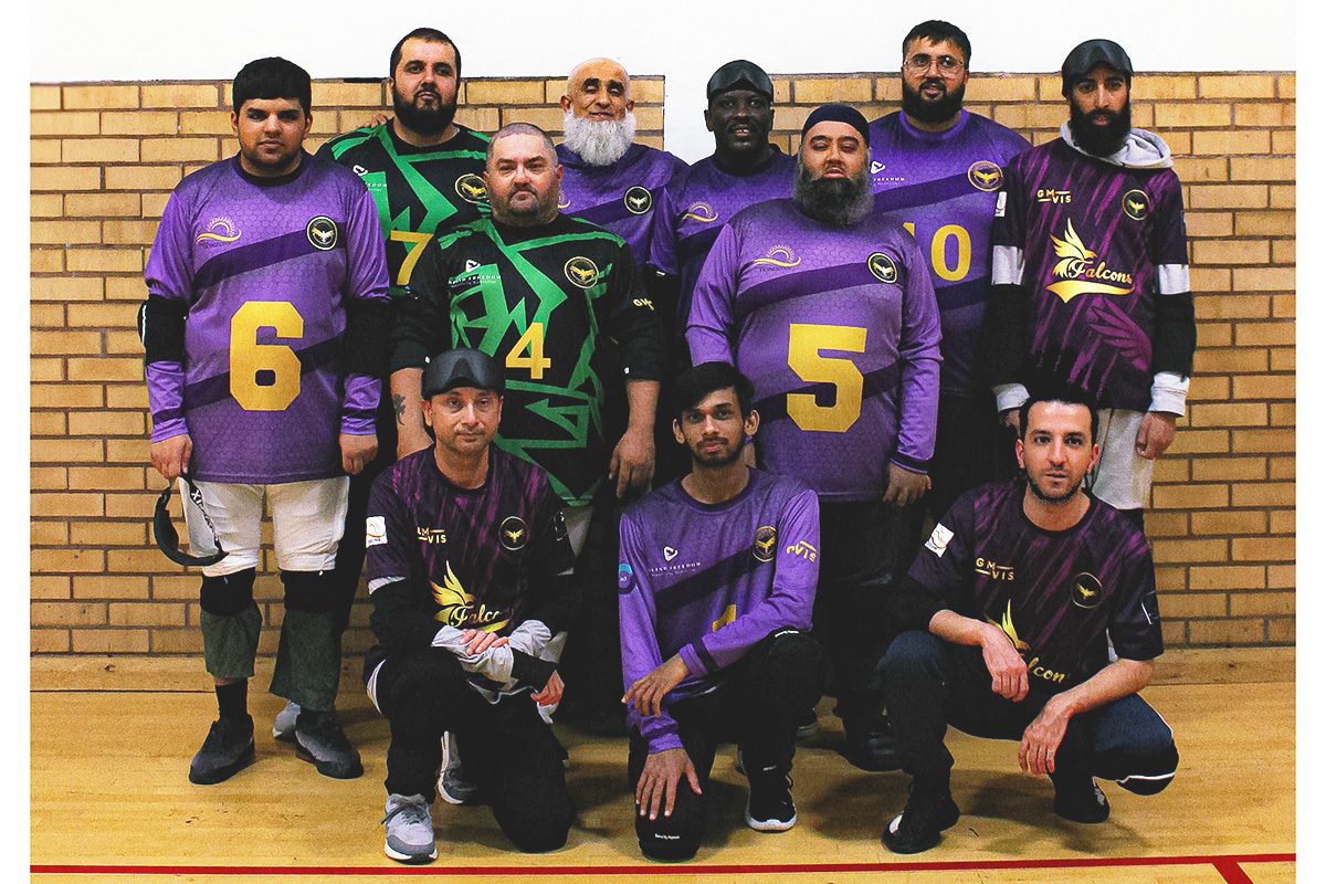 The Greater Manchester Vis goalball squad in purple and gold Falcons kit, lined up in two rows in a sports hall, several wearing black eyeshades.