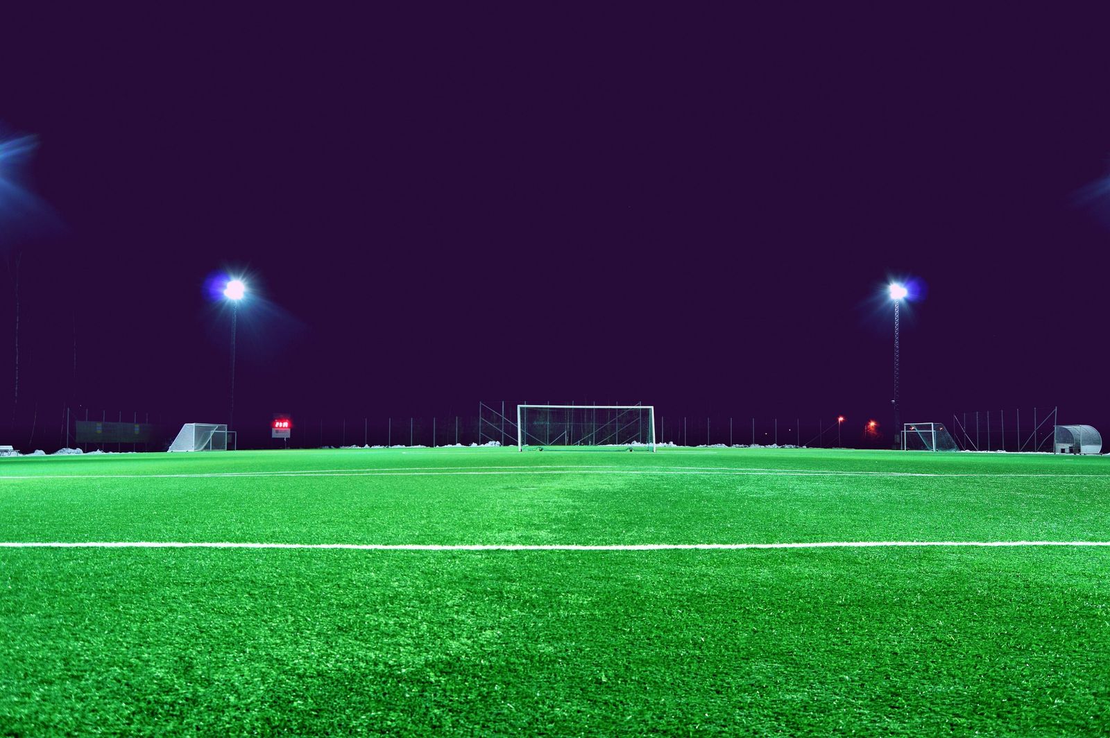 A floodlit artificial football pitch at night.